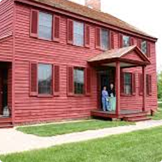 Red two-story house with people standing on the porch.