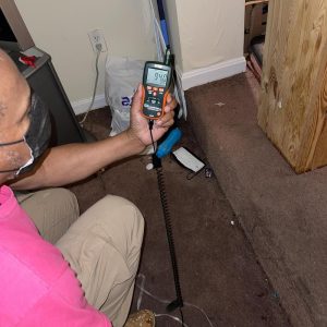 Technician using moisture meter to check carpet and wall for water damage during home restoration inspection