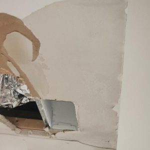 Damaged drywall with cut-out section exposing vent during interior repair and restoration work