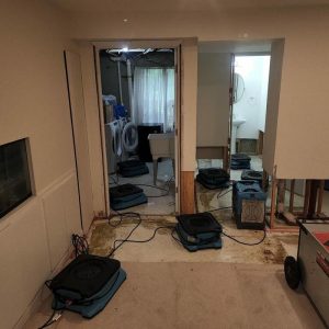 Room under renovation with exposed walls, drying fans, and restoration equipment on the floor.