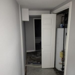 Utility hallway with water heater and damaged flooring after leak.