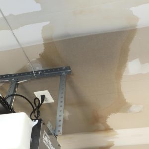 Water-stained garage ceiling with damp drywall around a metal support bracket.