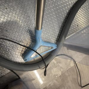 Water extraction wand and hose positioned on wet floor during cleanup.