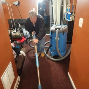 Technician extracting water from carpet using professional drying equipment during flood restoration process
