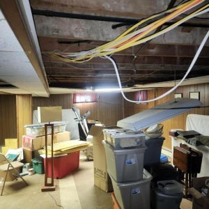 Basement with exposed ceiling wiring and stored items during inspection and renovation work