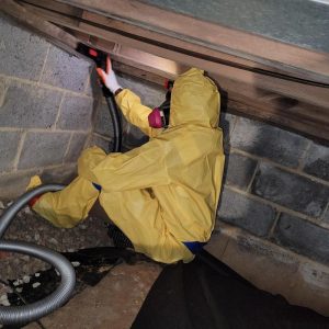 Worker in protective gear inspecting crawl space framing during contamination cleanup and remediation work