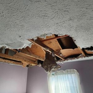 Bedroom ceiling with large hole and exposed wooden beams after water damage collapse