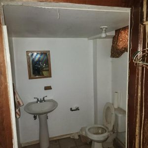 Small basement bathroom with damaged ceiling and exposed insulation after water damage