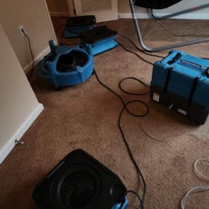 Multiple air movers and dehumidifier operating on carpet during indoor water damage drying process