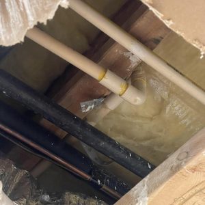 Ceiling opening with exposed plumbing pipes and insulation during water damage repair work