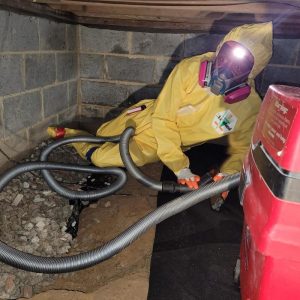 Technician in protective suit removing contaminated soil in crawl space during sewage cleanup and remediation