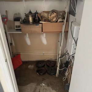 Water-damaged utility closet floor with sump pump covers and wiring.