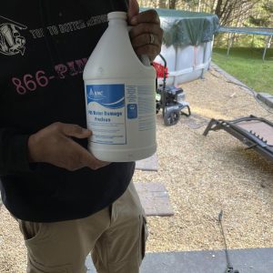 Technician holding a gallon container of antimicrobial disinfectant solution used for cleaning, sanitizing, and mold prevention during restoration work.
