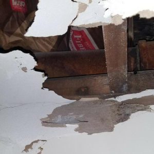 Ceiling drywall broken, exposing wooden beams above.