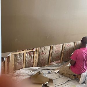 Technician removing lower drywall and insulation during water damage restoration process