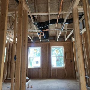 New home interior framing with exposed ceiling beams, ductwork, and twin windows during construction