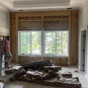 Basement renovation in progress with insulation removal, exposed wall framing, ladder setup, and debris pile near windows during water damage repair work