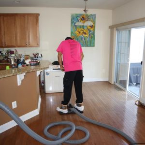 Water damage restoration technician extracting moisture from hardwood floors in a kitchen using professional drying equipment.