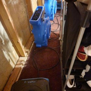 Alt tag: Air movers placed along hallway wall with exposed framing during water damage drying process