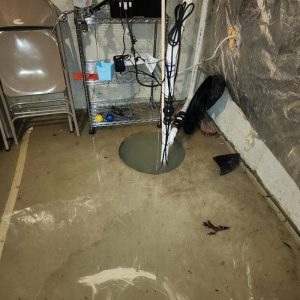 Basement sump pump pit with standing water on concrete floor after flooding