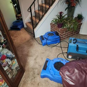 Air movers and dehumidifier set up in living room near staircase during water damage drying process