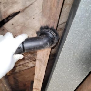 Close-up of technician vacuuming wall cavity around pipe during mold or contamination remediation work