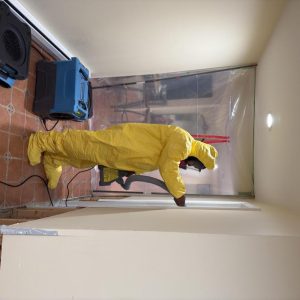 Technician in yellow protective suit walking through plastic containment during indoor restoration work.