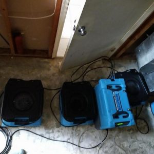 Water damage restoration equipment including commercial dehumidifier and air movers operating on basement floor during flood cleanup and drying process