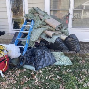 Pile of removed carpet and padding with debris bags outside home during water damage restoration cleanup