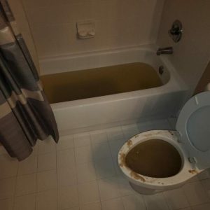 Bathroom flooded with brown water in bathtub and toilet during sewage backup cleanup