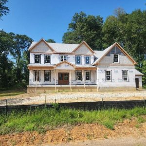Newly built single-family home under construction with exterior wrap and unfinished landscaping