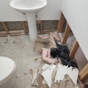 Bathroom with damaged walls and debris after water damage.
