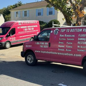 Two pink restoration service vans parked in a residential neighborhood.