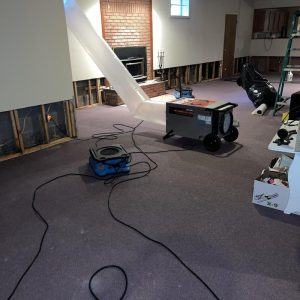 Basement water damage restoration in progress with drying equipment, generator, air mover hoses, and exposed lower wall framing after flood cleanup
