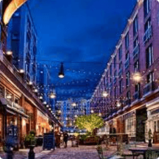 Outdoor shopping street lit with string lights at night.