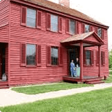 Red two-story house with people standing on the porch.