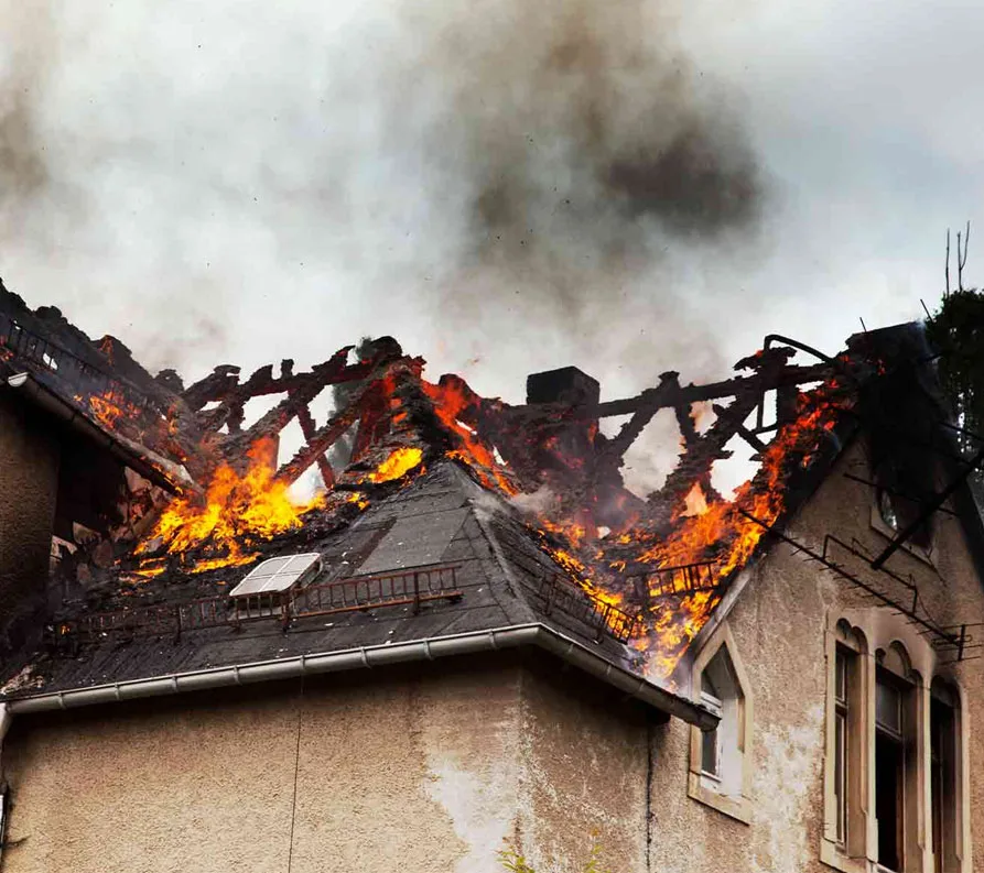 House roof damaged by fire with visible flames and smoke.